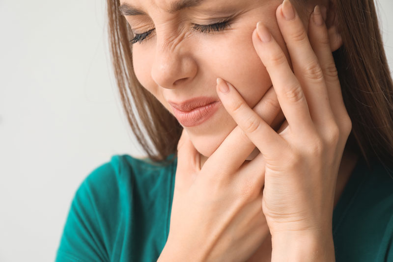 a dental patient holding her jaw and cheek in the area where she has peri-implantitis.